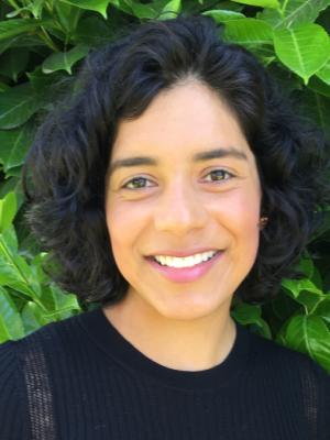 Woman with black hair and black sweater against green leafy background