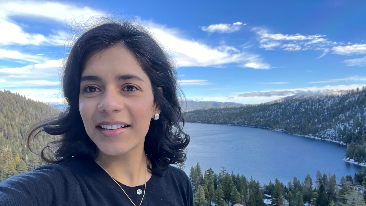 Magali Blanco looks to her right. Behind and below her is a lake surrounded by evergreens.