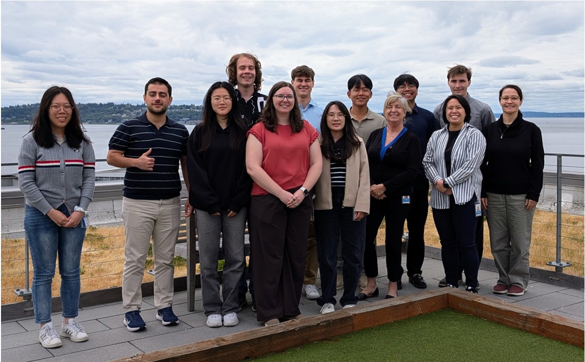 A group photo of 13 people on the deck of a ship with water in the background.