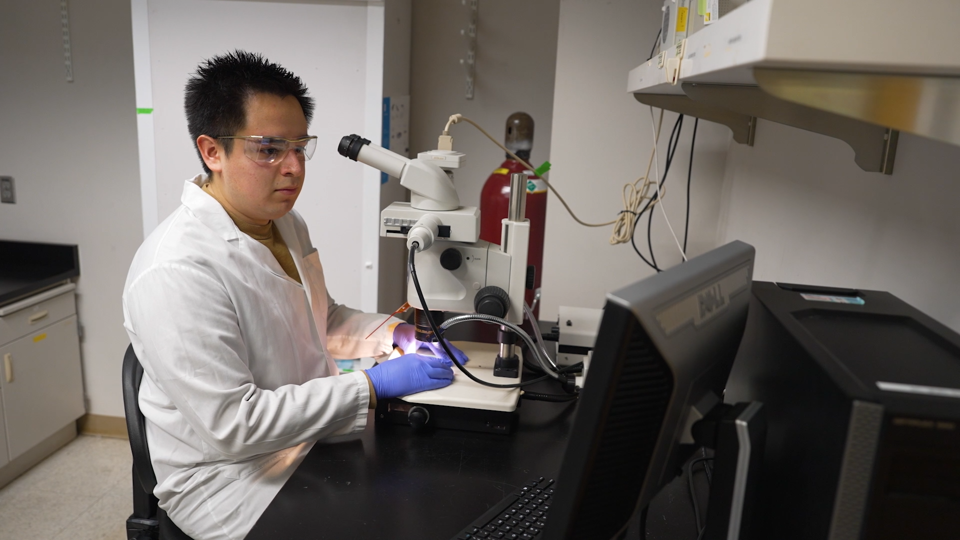 Leo Diaz sits at a desk looking at a microscope in the lab.
